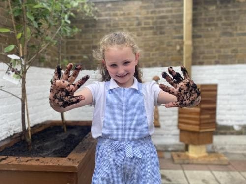 A pupil shows muddy hands while gardening in a photograph promoting Veolia Orchard